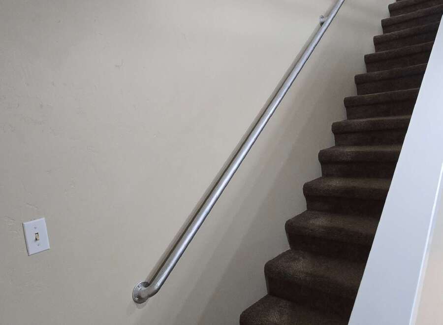 Enhance your home's safety and accessibility with this sturdy metal handrail, perfectly complementing the carpeted stairs.