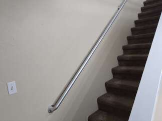 Enhance your home's safety and accessibility with this sturdy metal handrail, perfectly complementing the carpeted stairs.