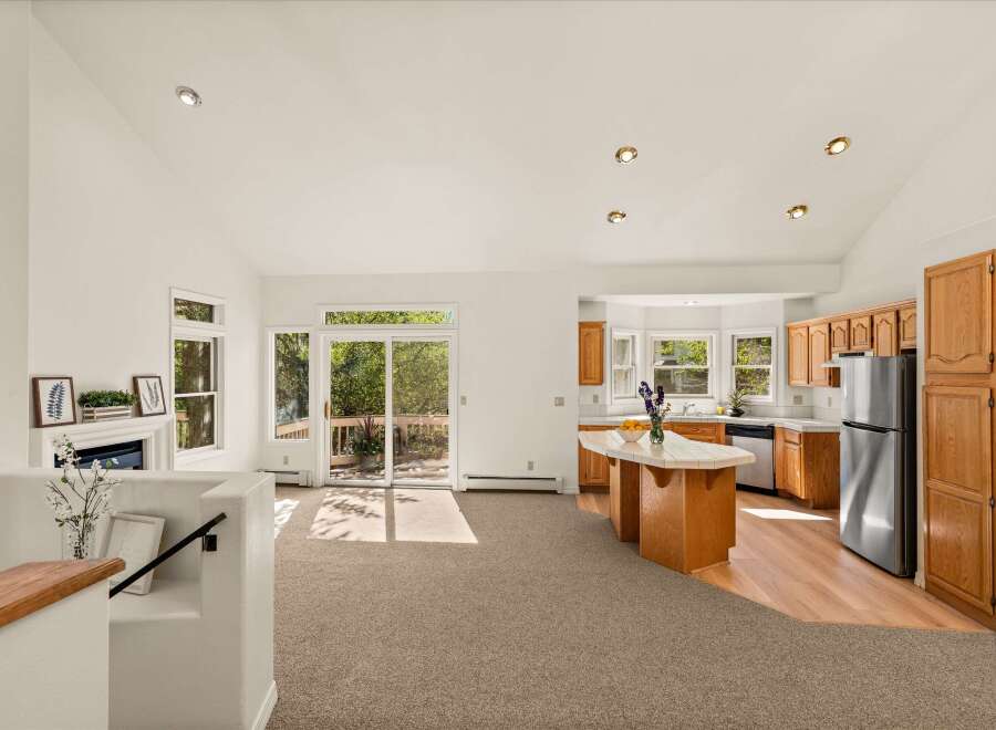 This spacious open-concept living area features a cozy fireplace, a large sliding glass door leading to an outdoor deck, and a well-appointed kitchen with a central island.