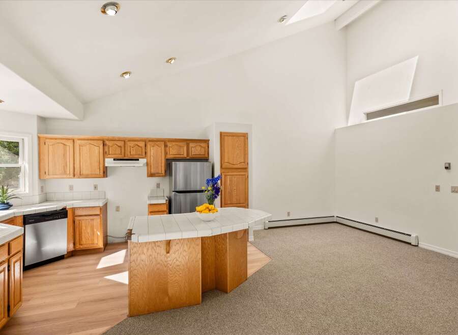 This spacious kitchen boasts ample natural light, complemented by warm wooden cabinetry and a tiled island perfect for meal prep and casual dining.