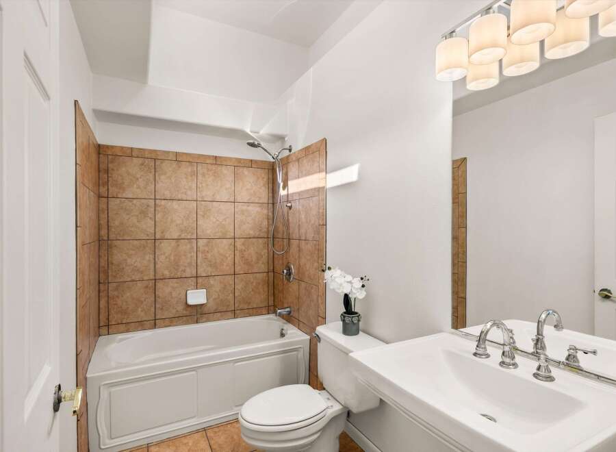 This bathroom features a classic white bathtub with a tiled surround, complemented by a white toilet and a spacious vanity with a double faucet.