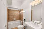 This bathroom features a classic white bathtub with a tiled surround, complemented by a white toilet and a spacious vanity with a double faucet.