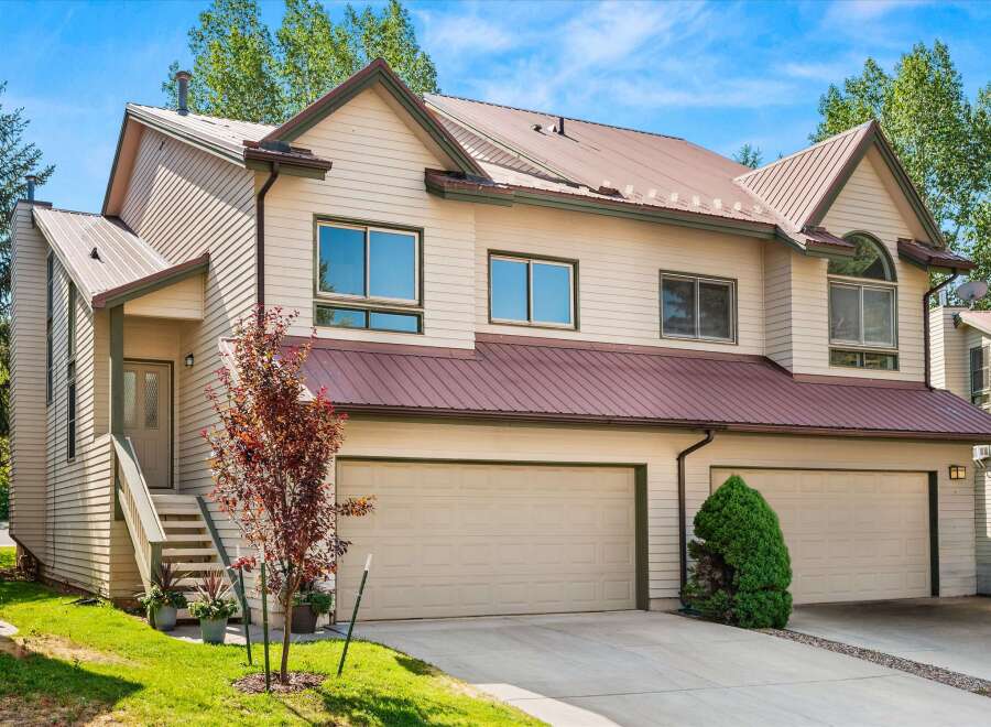 This charming townhouse features a light beige exterior with a durable, dark red metal roof.