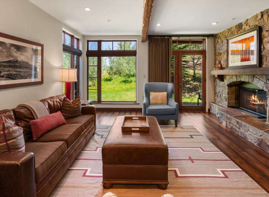 Experience rustic elegance in this inviting living room, featuring a plush leather sofa and a cozy armchair perfect for relaxing by the stone fireplace.