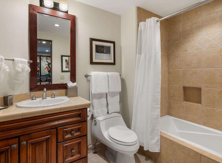 This charming bathroom features a spacious vanity with a granite countertop and a deep basin sink, complemented by a large wooden-framed mirror.