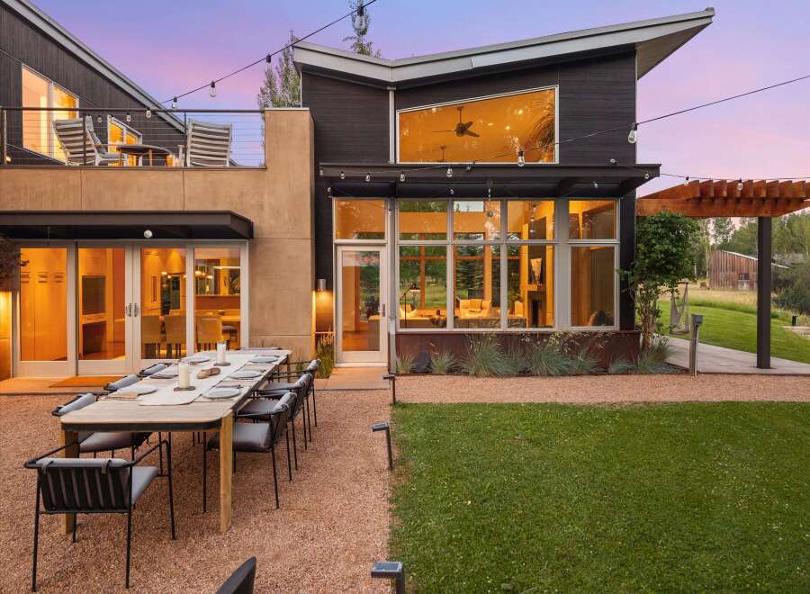 Experience luxurious outdoor living with this stunning modern home, featuring a spacious dining area set on a gravel patio, perfect for al fresco entertaining.