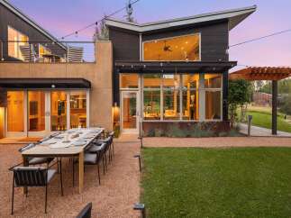 Experience luxurious outdoor living with this stunning modern home, featuring a spacious dining area set on a gravel patio, perfect for al fresco entertaining.