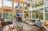 Experience modern living in this stunning great room, featuring a soaring ceiling and expansive windows that flood the space with natural light and offer breathtaking views of the surrounding nature.