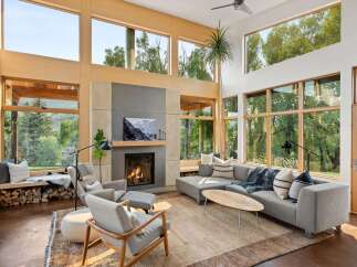 Experience modern living in this stunning great room, featuring a soaring ceiling and expansive windows that flood the space with natural light and offer breathtaking views of the surrounding nature.