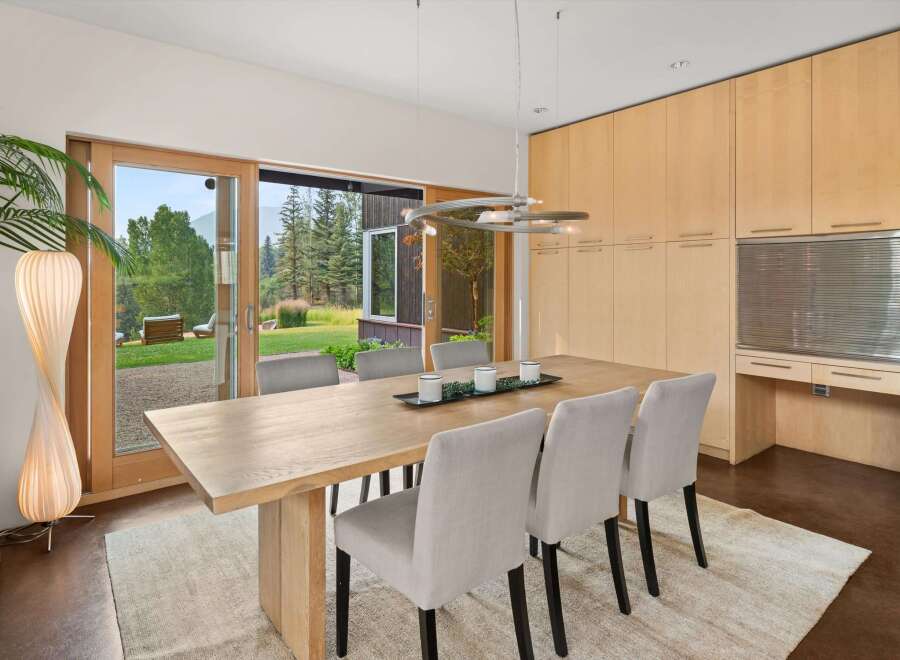 Experience seamless indoor-outdoor living in this elegant dining room, featuring a large wooden table and comfortable upholstered chairs.