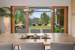 Experience seamless indoor-outdoor living with this stunning dining area featuring a large wooden table and chairs, opening up to a breathtaking mountain view.