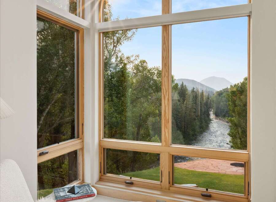 Experience breathtaking natural beauty from this stunning corner window, offering panoramic views of a serene river winding through lush forests and majestic mountains.