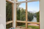 Experience breathtaking natural beauty from this stunning corner window, offering panoramic views of a serene river winding through lush forests and majestic mountains.