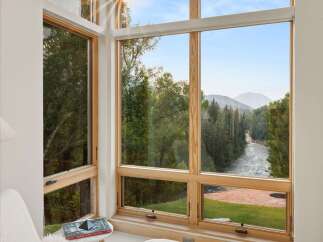 Experience breathtaking natural beauty from this stunning corner window, offering panoramic views of a serene river winding through lush forests and majestic mountains.