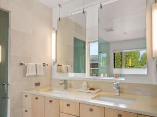 This modern bathroom features a double vanity with light wood cabinetry and a cream-colored countertop, complemented by sleek chrome fixtures.