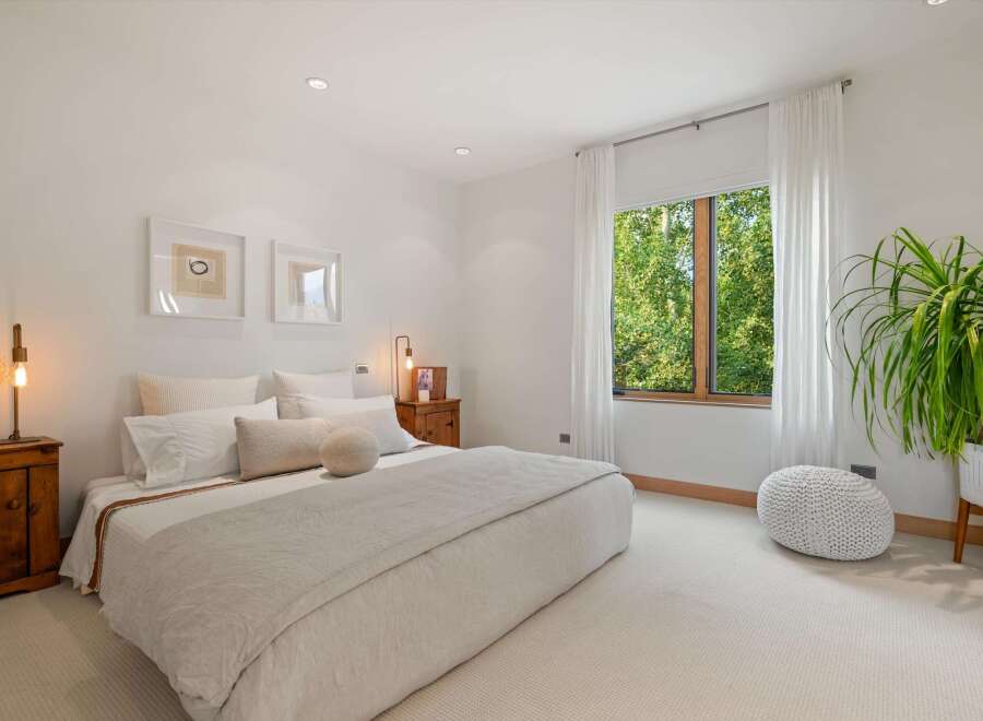 Experience serene living in this beautifully appointed bedroom, featuring a plush bed, elegant artwork, and a large window offering lush green views.