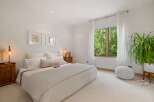 Experience serene living in this beautifully appointed bedroom, featuring a plush bed, elegant artwork, and a large window offering lush green views.
