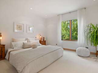 Experience serene living in this beautifully appointed bedroom, featuring a plush bed, elegant artwork, and a large window offering lush green views.