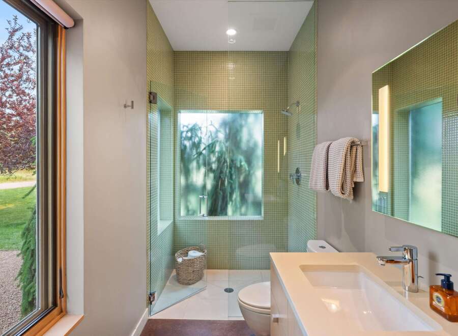 Experience modern luxury in this stunning bathroom featuring a walk-in shower with elegant green mosaic tile and a frosted glass window offering a serene view.