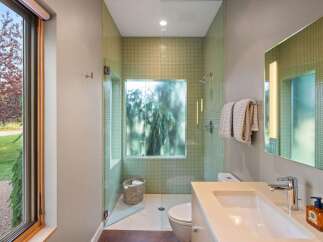 Experience modern luxury in this stunning bathroom featuring a walk-in shower with elegant green mosaic tile and a frosted glass window offering a serene view.