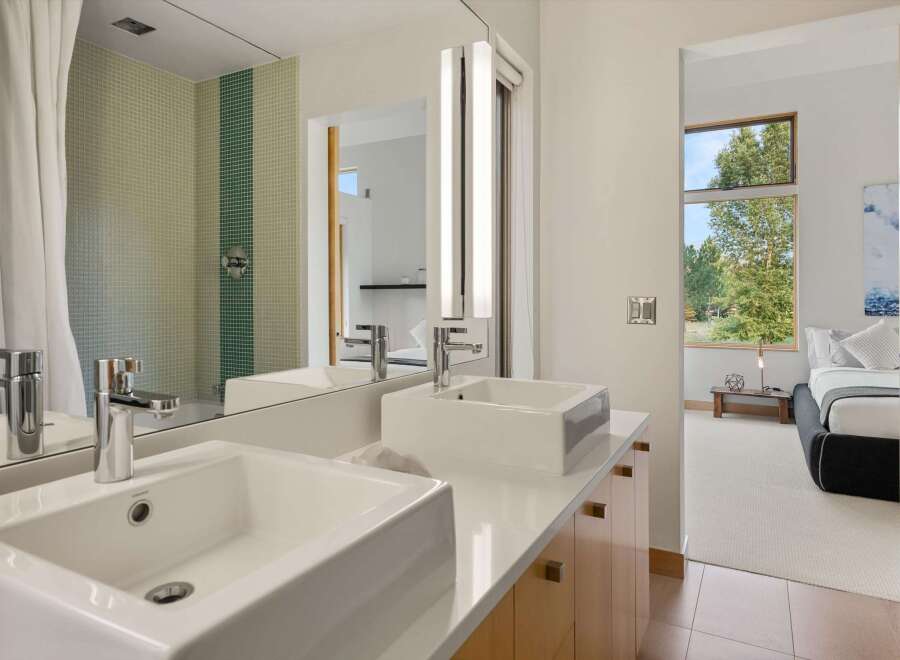 Experience modern luxury in this stunning bathroom featuring dual vessel sinks atop a sleek white countertop and complemented by a vibrant mosaic tile shower.