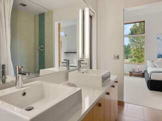 Experience modern luxury in this stunning bathroom featuring dual vessel sinks atop a sleek white countertop and complemented by a vibrant mosaic tile shower.