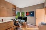 This modern home office features a sleek built-in wooden cabinetry system with ample storage, complemented by a spacious desk equipped with dual monitors.