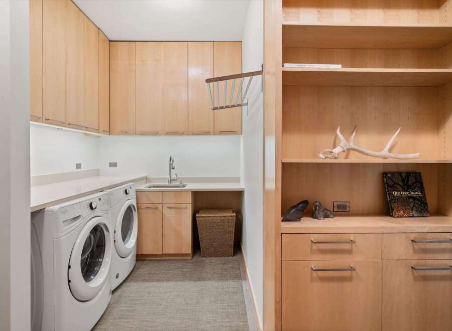 This laundry room boasts ample storage with light wood cabinetry and open shelving.