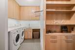 This laundry room boasts ample storage with light wood cabinetry and open shelving.