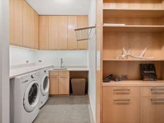 This laundry room boasts ample storage with light wood cabinetry and open shelving.
