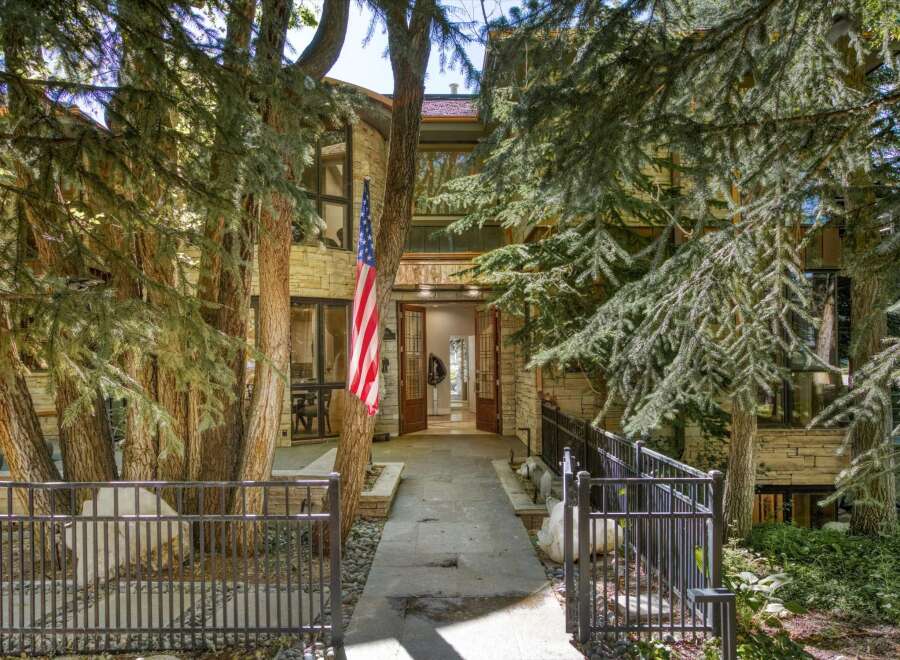 This stunning home features a grand entrance with double doors, flanked by mature trees and a welcoming American flag.