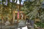This stunning home features a grand entrance with double doors, flanked by mature trees and a welcoming American flag.