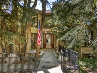 This stunning home features a grand entrance with double doors, flanked by mature trees and a welcoming American flag.