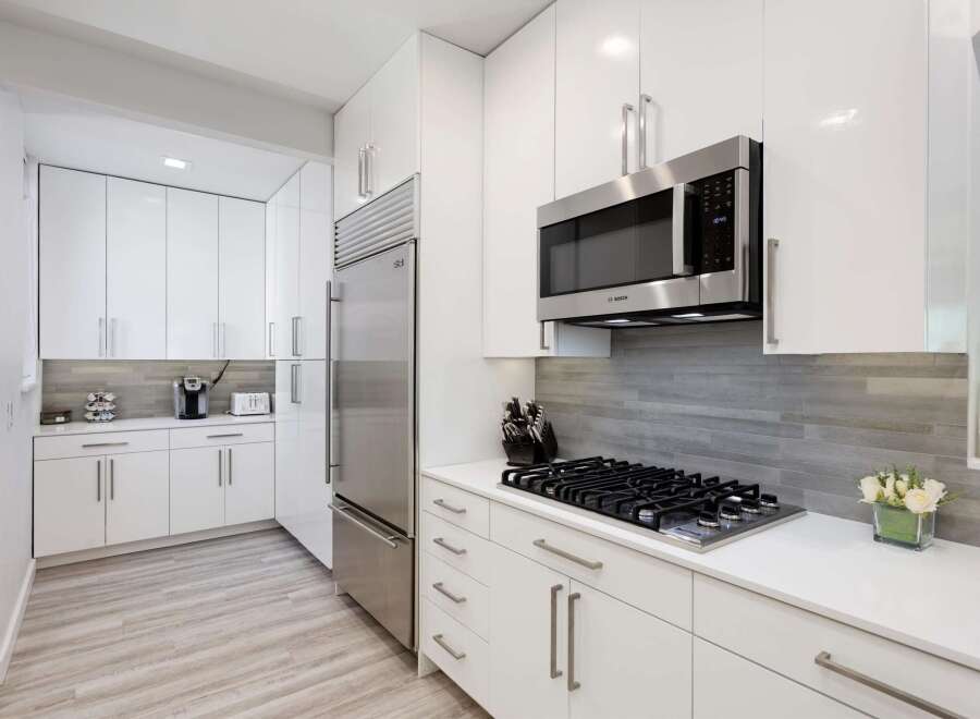 Experience modern living in this sleek white kitchen, featuring high-end stainless steel appliances including a built-in microwave and a spacious refrigerator.