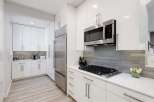 Experience modern living in this sleek white kitchen, featuring high-end stainless steel appliances including a built-in microwave and a spacious refrigerator.