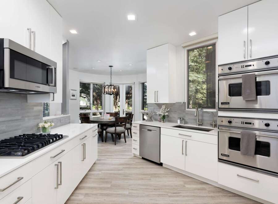 Experience modern luxury in this stunning kitchen, featuring sleek white cabinetry, a sophisticated grey tile backsplash, and top-of-the-line stainless steel appliances including a Bosch microwave and Viking double ovens.