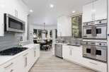 Experience modern luxury in this stunning kitchen, featuring sleek white cabinetry, a sophisticated grey tile backsplash, and top-of-the-line stainless steel appliances including a Bosch microwave and Viking double ovens.