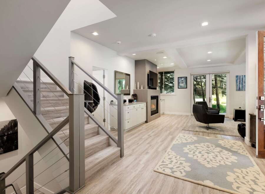 Step into this modern living space featuring a sleek staircase with cable railings and a cozy fireplace area.