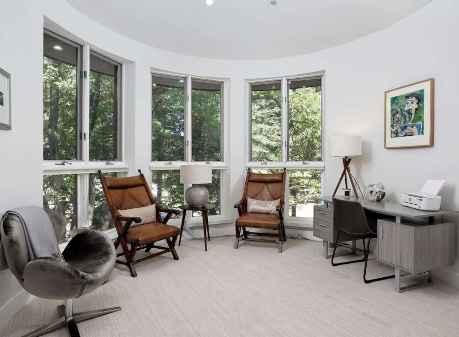 This bright and airy room features a curved wall of windows offering serene views of the surrounding trees.