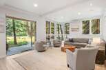 Step into this inviting living room, bathed in natural light from large windows overlooking a serene wooded landscape.