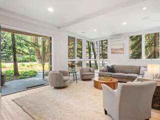 Step into this inviting living room, bathed in natural light from large windows overlooking a serene wooded landscape.