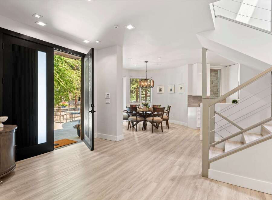 Step into this stunning modern entryway featuring a grand black pivot door that opens to a lush outdoor patio.