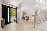 Step into this stunning modern entryway featuring a grand black pivot door that opens to a lush outdoor patio.