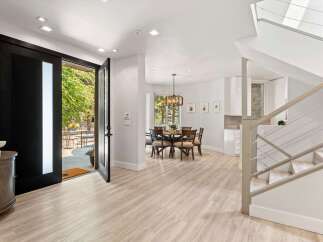 Step into this stunning modern entryway featuring a grand black pivot door that opens to a lush outdoor patio.