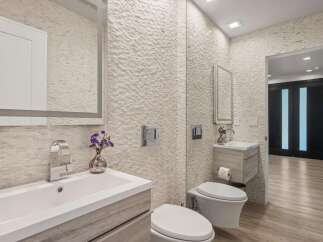 Experience modern luxury in this stunning bathroom, featuring a sleek vanity with a waterfall faucet and a unique textured stone accent wall.