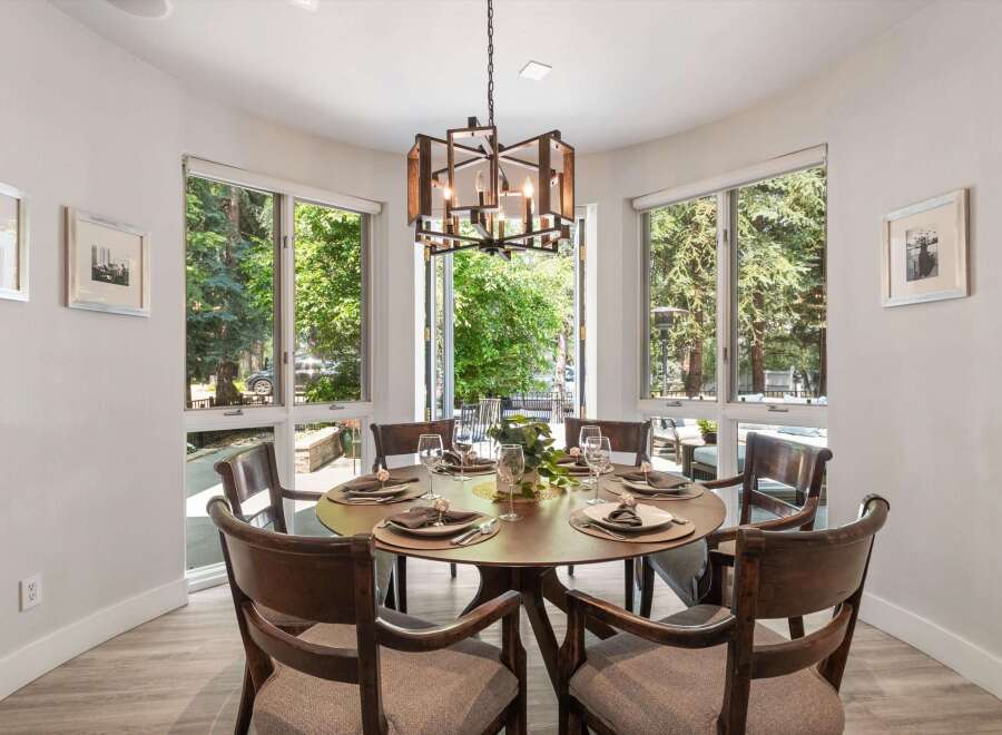 Dine in style in this elegant dining room, featuring a round wooden table set for six and surrounded by large windows that offer a lush green view.