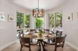 Dine in style in this elegant dining room, featuring a round wooden table set for six and surrounded by large windows that offer a lush green view.