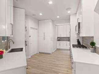 Experience modern living in this sleek, white galley kitchen featuring high-gloss cabinetry and a durable quartz countertop.