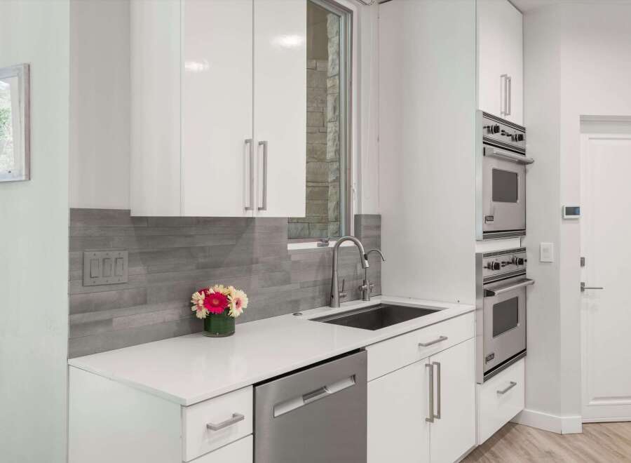 This modern kitchen features sleek white cabinetry and a stylish grey tiled backsplash.