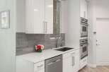 This modern kitchen features sleek white cabinetry and a stylish grey tiled backsplash.